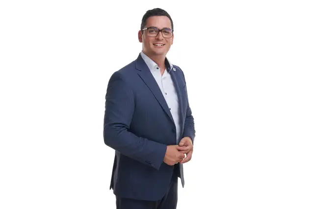 Mann mit Brille im blauen Anzug und weißem Hemd, lächelnd vor weißem Studiohintergrund, Business-Portrait in Dreiviertelansicht