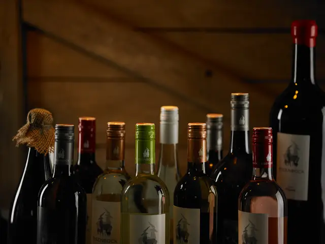 Weinsortiment eines Weinguts vor dunkler Holzwand, Weiß-, Rosé- und Rotweinflaschen gestaffelt aufgestellt