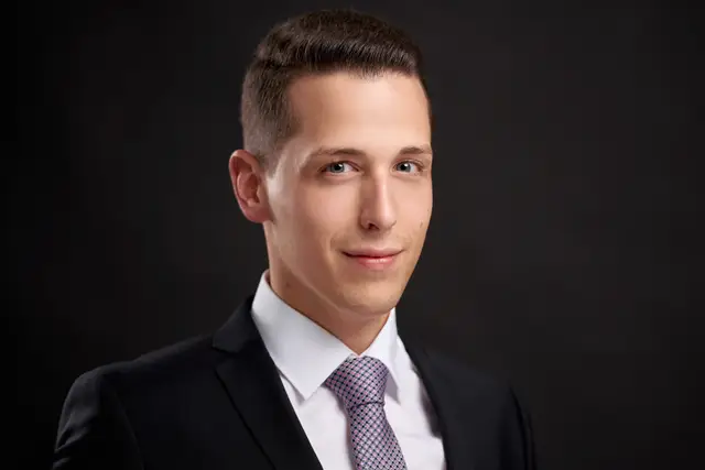 Junger Mann im dunklen Anzug mit Krawatte, klassisches Businessportrait vor schwarzem Hintergrund