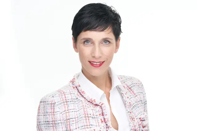 Business-Portrait einer Managerin mit dunklem Kurzhaarschnitt in Bluse und Tweed-Blazer vor weißem Hintergrund