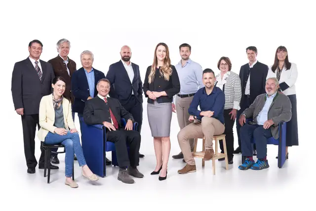 Gruppenfoto von rund einem Dutzend Mitarbeitenden vor weißem Studiohintergrund, teils sitzend, teils stehend