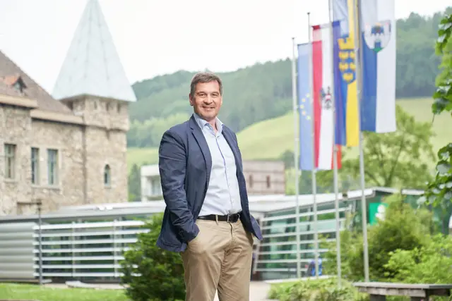 Bürgermeister-Portrait im blauen Sakko vor Kirchturm und Fahnenmasten im Ortszentrum
