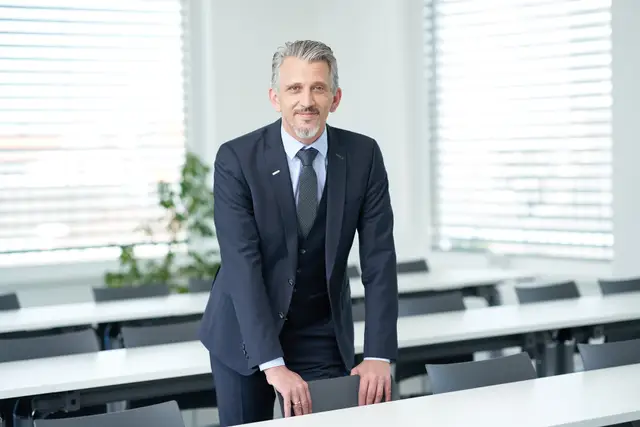 Führungskräfte-Portrait eines Managers im dreiteiligen Anzug, locker an einen Stuhl im Seminarraum gelehnt