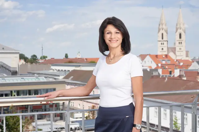 Führungskraft im weißen Shirt auf einer Dachterrasse, im Hintergrund Altstadtdächer und Kirchtürme