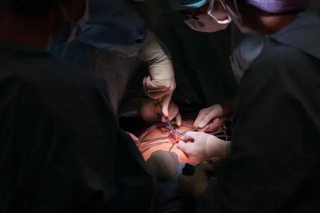 Chirurgisches Team bei einer Operation im abgedunkelten OP-Saal, konzentrierte Handgriffe im OP-Licht
