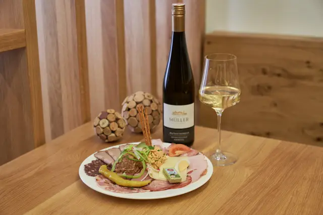 Gedeckter Heurigentisch mit Brettljause, Weinflasche und einem Glas Weißwein aus Eichenholz