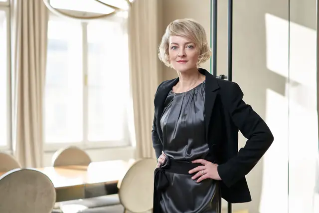 Selbstbewusste Managerin in schwarzem Blazer und Seidenkleid, Hand in der Hüfte, im eleganten hellen Büro