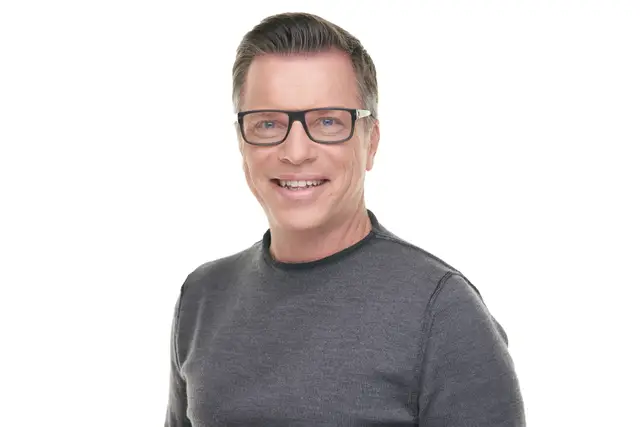 Junger blonder Mann mit Dreitagebart im dunkelblauen Sakko und weißem Hemd, Studio-Portrait vor hellem Hintergrund