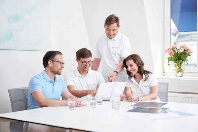 Ärzteteam im hellen Besprechungsraum der Ordination, gemeinsamer Blick auf Befunde