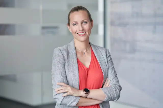 Freundlich lächelnde Führungskraft im grauen Blazer mit verschränkten Armen im modernen Büro
