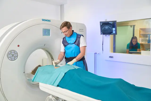 Radiologe mit Strahlenschutzweste bei einer CT-gestützten Behandlung im Krankenhaus