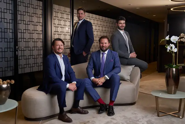 Vier Geschäftspartner in Anzügen auf heller Sitzbank in eleganter Lounge – repräsentatives Imagefoto