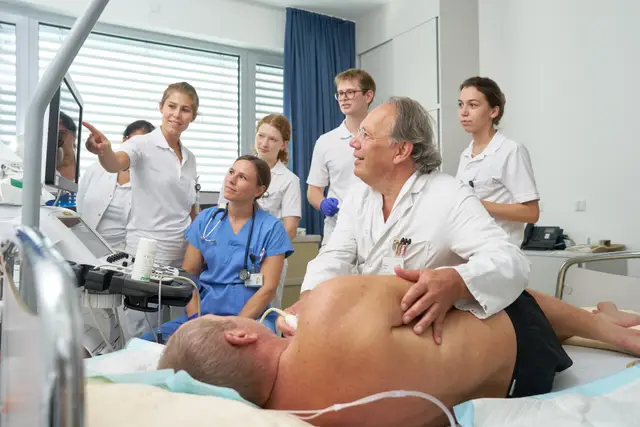Erfahrener Arzt zeigt Studierenden die Ultraschalluntersuchung am Krankenbett, Lehrvisite in der Klinik