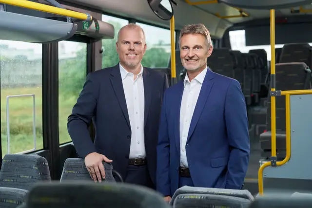 Zwei Geschäftsführer in Anzügen stehen lächelnd im Inneren eines Linienbusses ihres Unternehmens