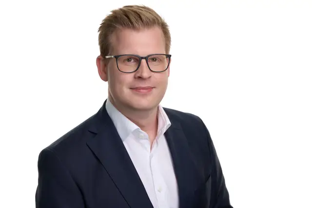 Blonder Mann mit Brille in dunklem Sakko, aktuelles Mitarbeiterfoto vor weißem Hintergrund