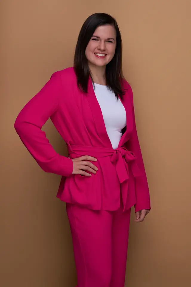 Junge Frau im pinken Hosenanzug mit weißem Top, Hand an der Hüfte, strahlendes Studio-Portrait vor beigem Hintergrund