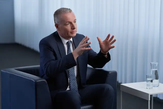 Manager im dunkelblauen Anzug erklärt gestikulierend im Ledersessel – Businessportrait im Interview-Setting