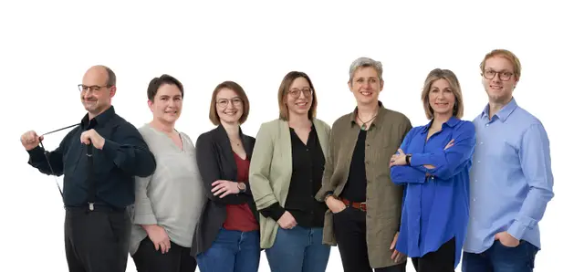 Sieben Kolleginnen und Kollegen in Business-Casual, einheitlich fotografiertes Teamfoto vor weißem Hintergrund