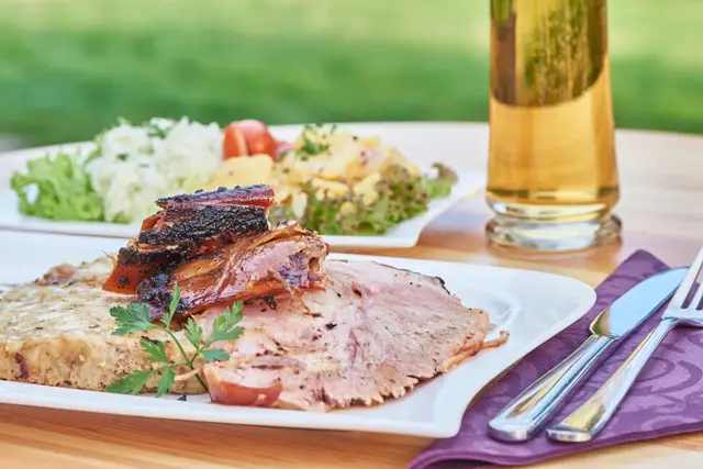 Knuspriger Schweinsbraten mit Salat und kühlem Bier auf dem Gastgartentisch, sommerliche Wirtshausküche