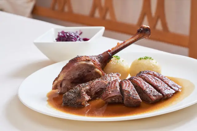 Knusprig gebratene Ente mit Kartoffelknödeln und Rotkraut auf weißem Teller im Wirtshaus