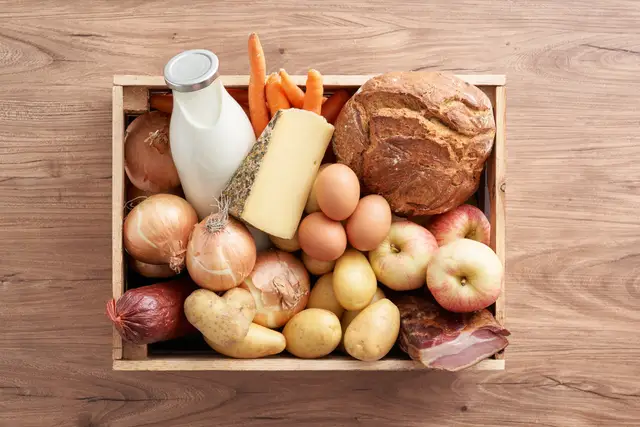 Holzkiste voll regionaler Lebensmittel: Brot, Milch, Käse, Eier, Gemüse und Speck von oben fotografiert