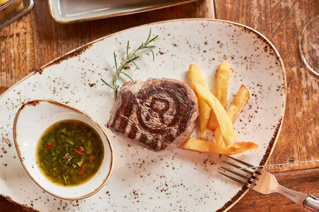 Gegrilltes Steak mit Chimichurri-Dip und Pommes auf rustikalem Teller, Foodfotografie von oben