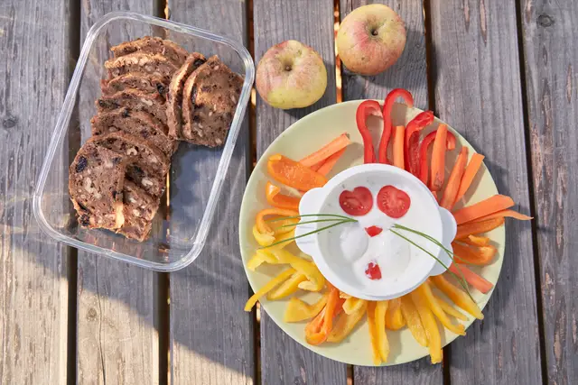Gesunde Jause für Kinder: Gemüsesticks mit lustig dekoriertem Joghurtdip und Früchtebrot im Freien