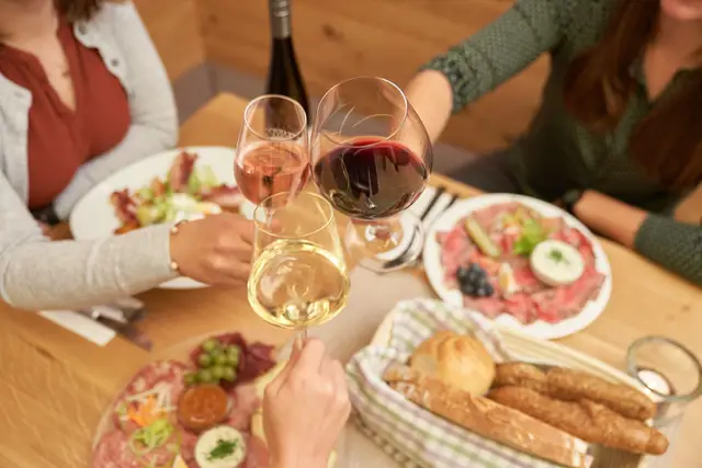 Gäste stoßen mit Weißwein, Rosé und Rotwein über Brettljause und Brotkorb an, Genussmoment von oben