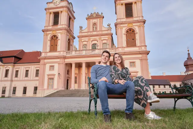 Junges Paar sitzt am Abend auf einer Parkbank vor der barocken Stiftskirche, entspannter Moment