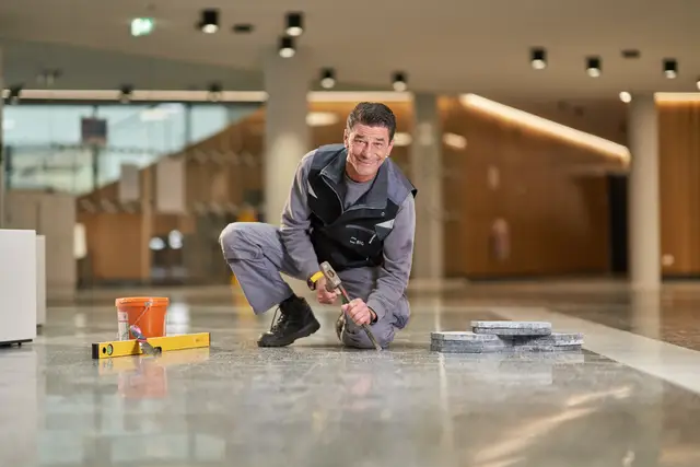Facharbeiter setzt kniend Steinplatten im Foyer eines Bürogebäudes, Imagefoto aus dem Gebäudeservice