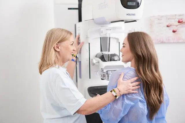 Radiologieassistentin begleitet eine Patientin einfühlsam zur Mammographie in der Ordination