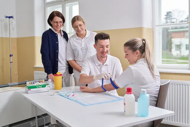 Pflegeschüler üben die Blutabnahme unter Anleitung, Ausbildungsalltag im Schulungsraum