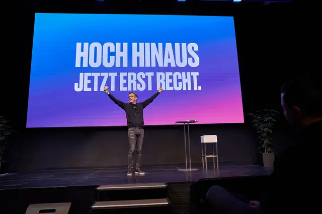 Keynote-Speaker jubelt auf der Bühne vor der Leinwand mit dem Motto Hoch hinaus, Eventreportage
