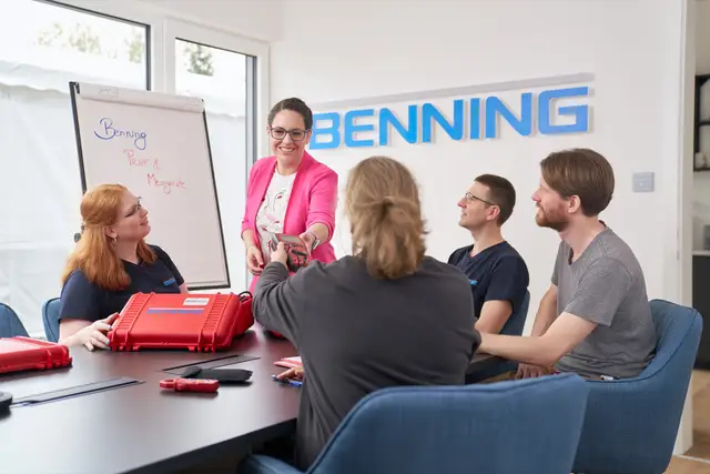 Produktschulung im Besprechungsraum: Trainerin reicht ein Messgerät über den Tisch, das Team hört zu