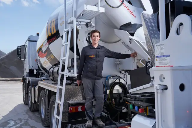 Junger Lenker steht stolz am Heck seines Fahrmischers im Schotterwerk, Imagefoto vom Betonwerk