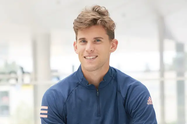 Junger Sportler im blauen Trainingsshirt lächelt entspannt in hellem, lichtdurchflutetem Gebäude, natürliches Portrait