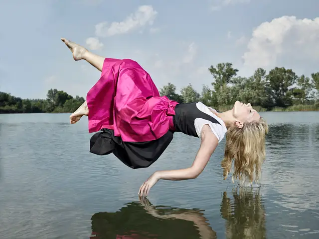 Schwebende Frau in pinkem Kleid über einem See, surreale Levitationsaufnahme mit Spiegelung im Wasser