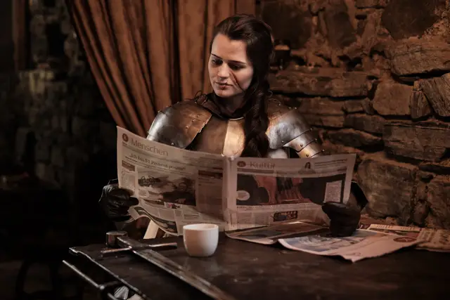 Ritterin in glänzender Rüstung liest Zeitung beim Kaffee in einer Burgstube, anachronistische Bildidee mit Augenzwinkern